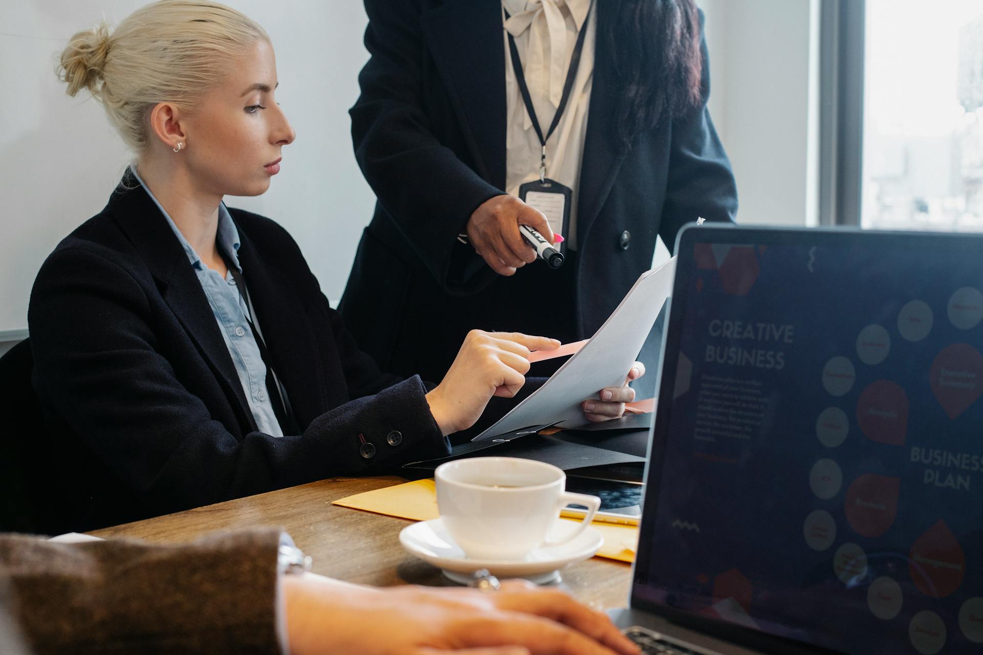 Group of young coworkers in formal wear gathering at table and discussing details of business plan in modern workspace