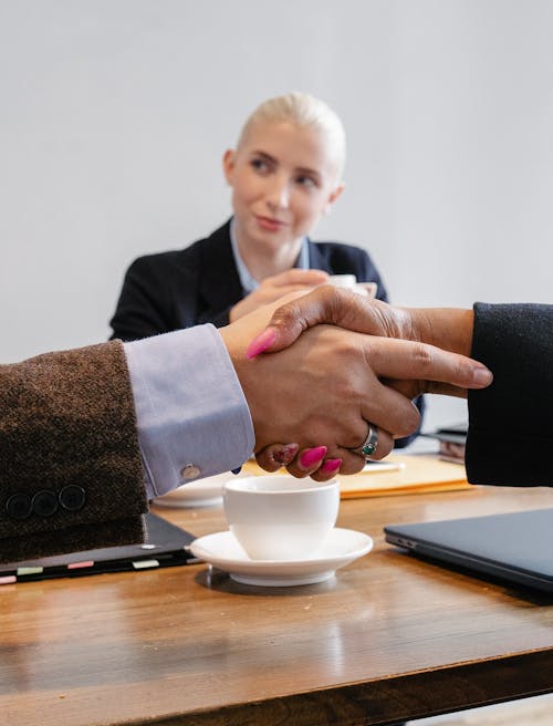 Free Crop faceless multiracial coworkers sitting at table and shaking hands after successful agreement in workspace Stock Photo