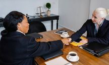 在摆着咖啡和笔记本的桌子旁，参加正式会议的女商人正在握手