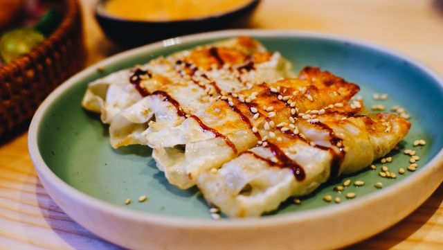 Close-up of appetizing gyoza dumplings garnished with sesame seeds and sauce, served on a plate.