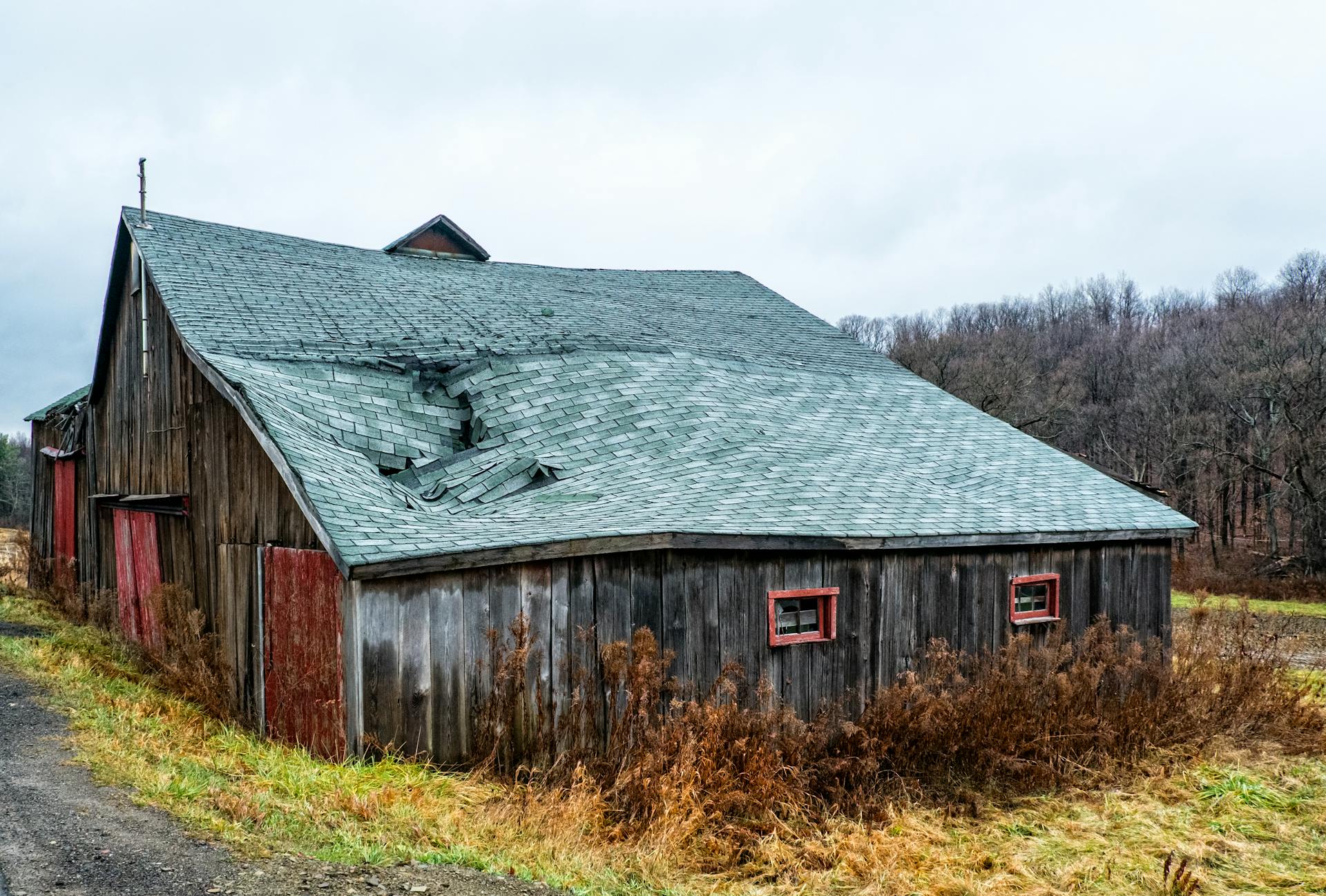 A weathered wooden barn with a damaged roof in a rural New York landscape.