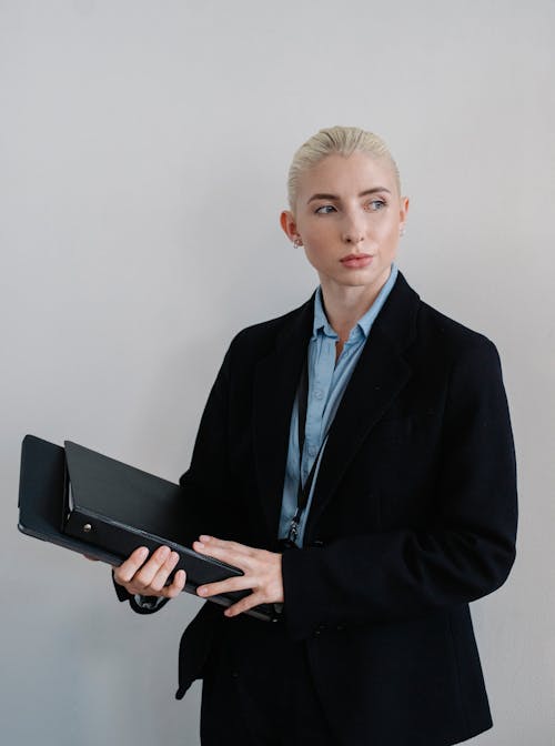 Positive businesswoman standing with folders against white wall
