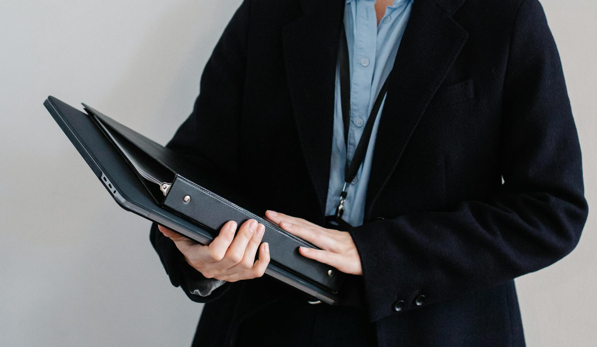 Crop unrecognizable professional office worker in formal clothes standing against white wall with folders in hands