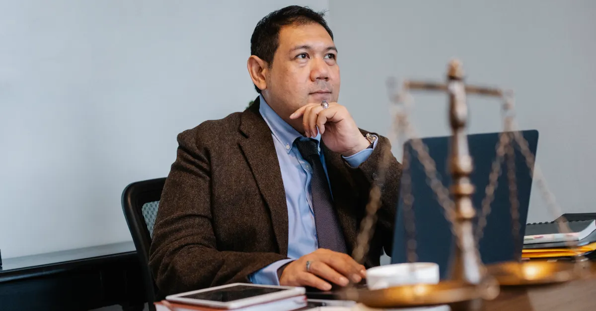 A lawyer in a formal suit reviewing case material on a laptop at a desk