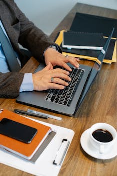 A business professional typing on a laptop at a neatly organized desk with coffee.