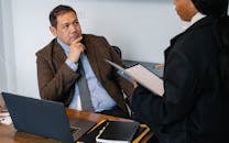 African American female office worker reading report for Asian male manager while working together in contemporary workspace