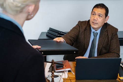 Concentrated ethnic businessman giving folder to female employee in workplace