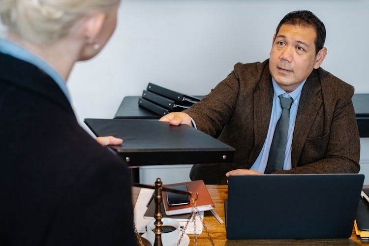 Concentrated Ethnic Businessman Giving Folder To Female Employee In Workplace