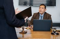 Crop unrecognizable employee representing new case details to concentrated middle aged ethnic lawyer sitting at table with laptop gavel and justice scales