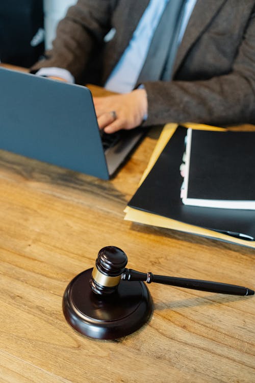 Free From above of crop anonymous male lawyer in formal clothes typing on laptop while sitting at wooden table with stack of documents and gavel Stock Photo