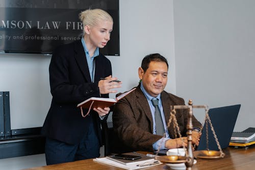 Ethnic male lawyer showing document on laptop to young female colleague