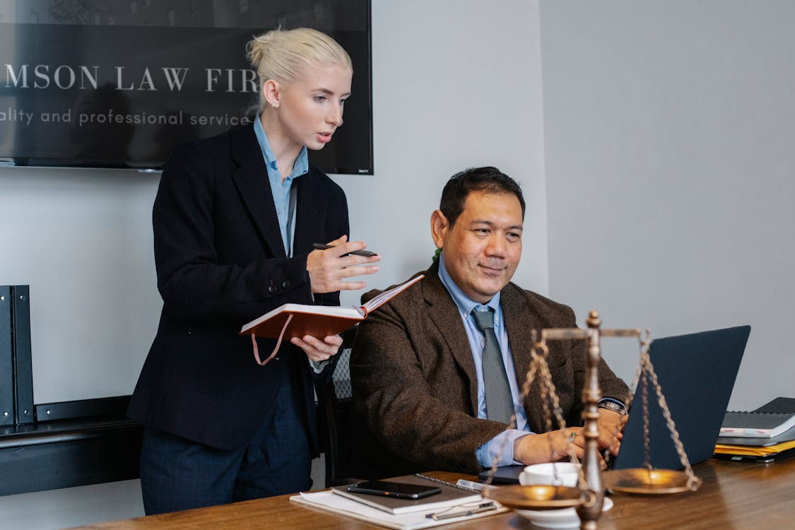 Free Ethnic male lawyer showing document on laptop to young female colleague Stock Photo