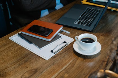 Free From above of opened laptop with cup of coffee placed on wooden table near notebooks and smartphone in office Stock Photo