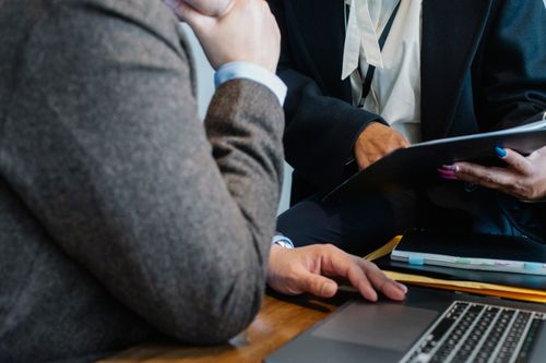 Free Crop faceless ethnic female entrepreneur in classy suit showing document to anonymous male boss sitting at table with laptop Stock Photo