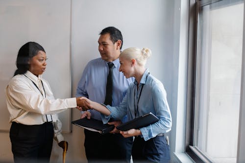 Happy young multiethnic female managers in classy outfits smiling and shaking hands during meeting with ethnic colleague in office