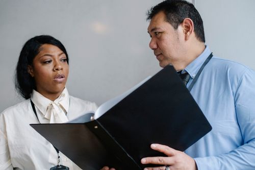 Free Serious middle aged male manager in shirt showing folder with documents to attentive female African American colleague during work in modern office Stock Photo