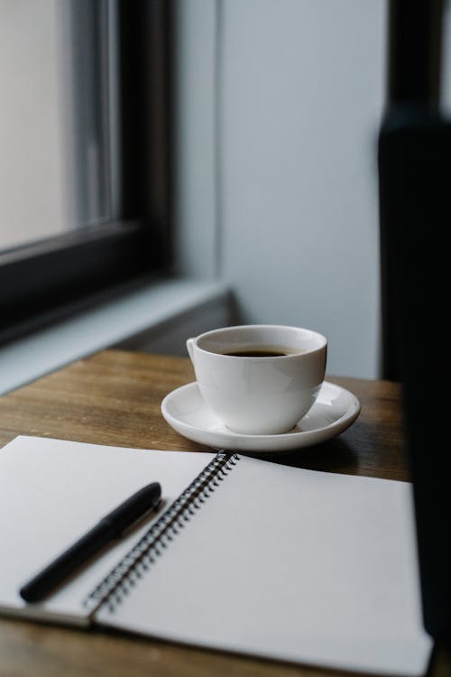 Cup of coffee served on table with notepad and pen