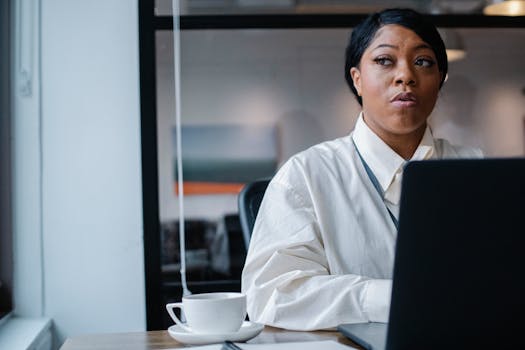 An African American woman in formal attire working on a laptop in an office setting.