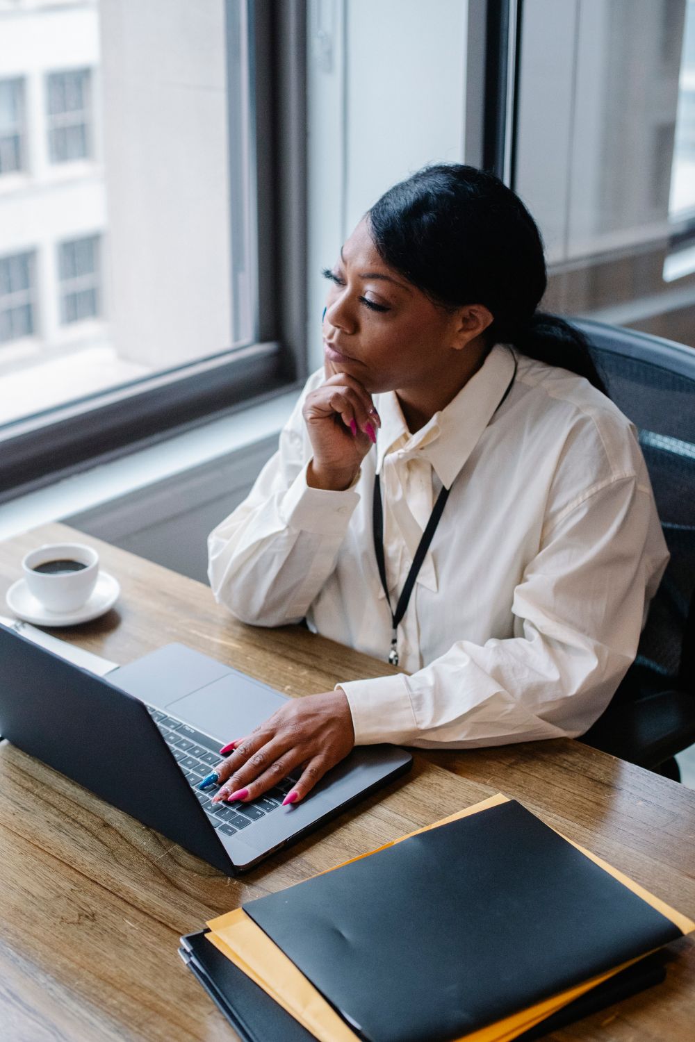 Pensive woman working on laptop in modern workplace · Free Stock Photo