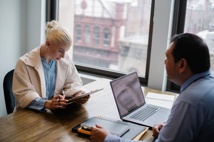 Serious Young Woman Reading Report To Colleague In Contemporary Workspace