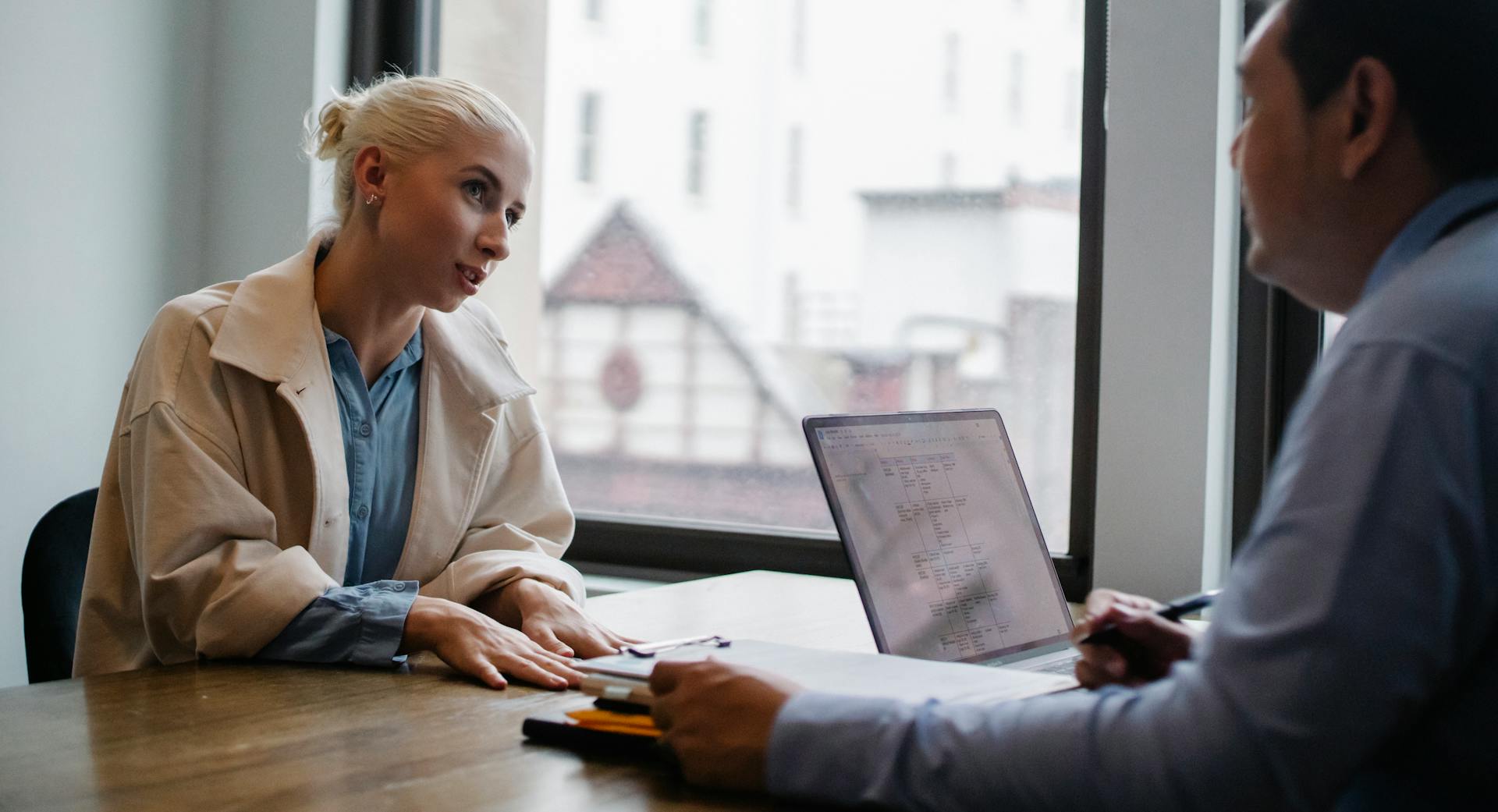 Two professionals engaged in a discussion at an office with a laptop and documents on the table.