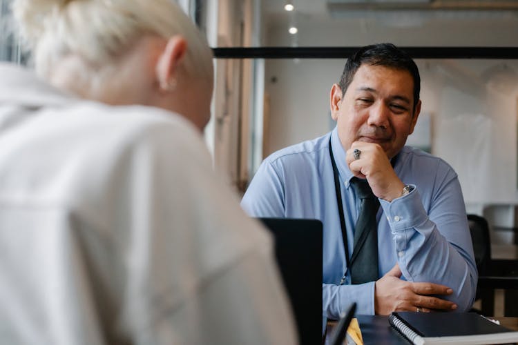 Positive Ethnic Manager Looking At Client Sitting In Office