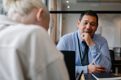 Free Confident ethnic male employee sitting at contemporary workplace and looking satisfied while young male client sitting in front Stock Photo