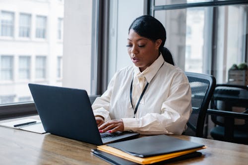 Serious black businesswoman typing text on laptop