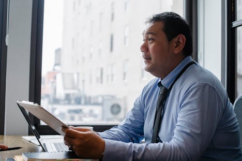 Free Side view of ethnic male boss with clipboard at table with modern gadget near window Stock Photo