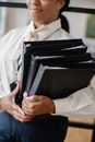 室内，一位穿着正式服装的职业女性正携带着多个黑色文件夹