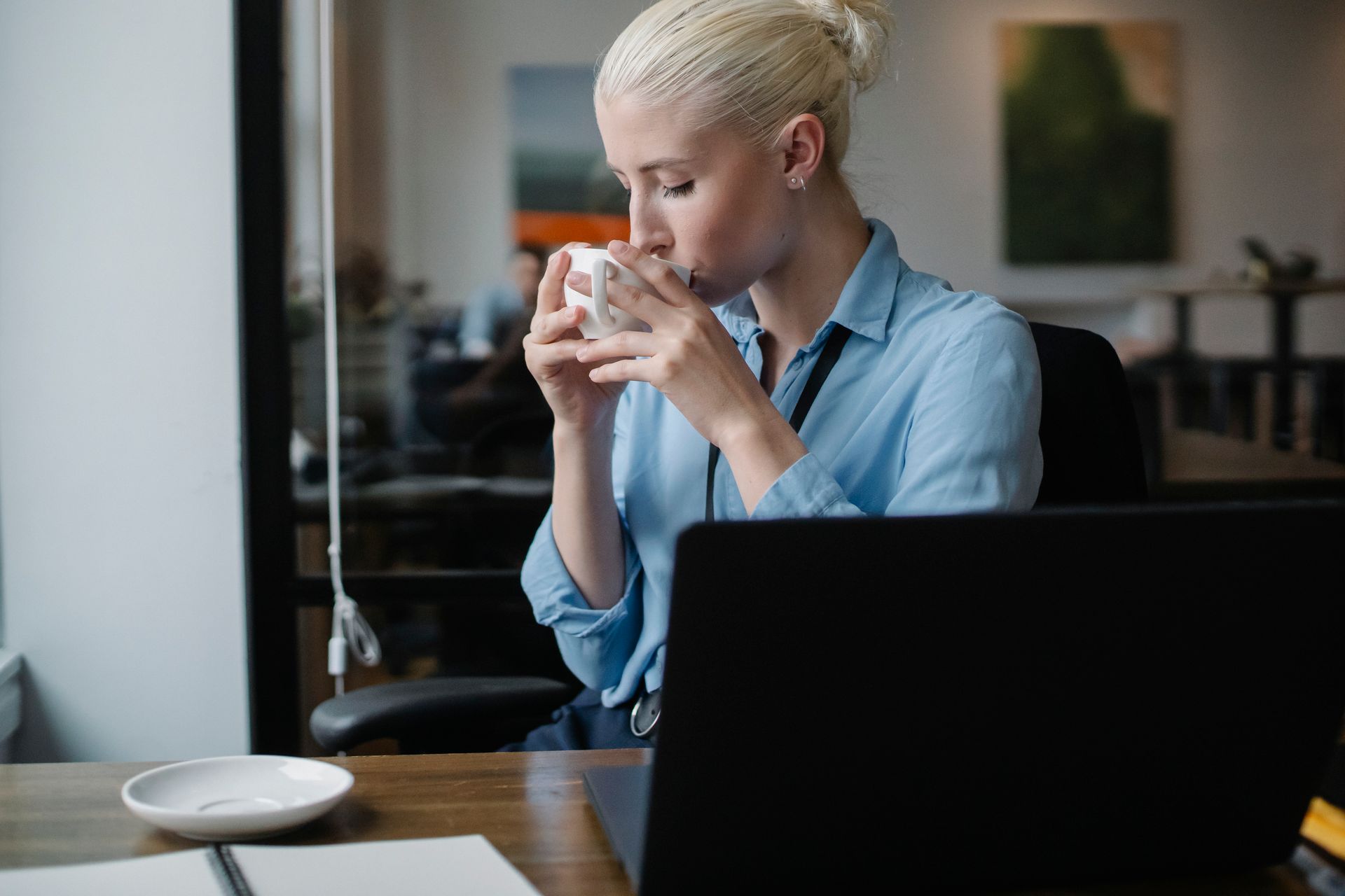 A professional woman takes a moment to enjoy a coffee during a work break in a modern office setting.