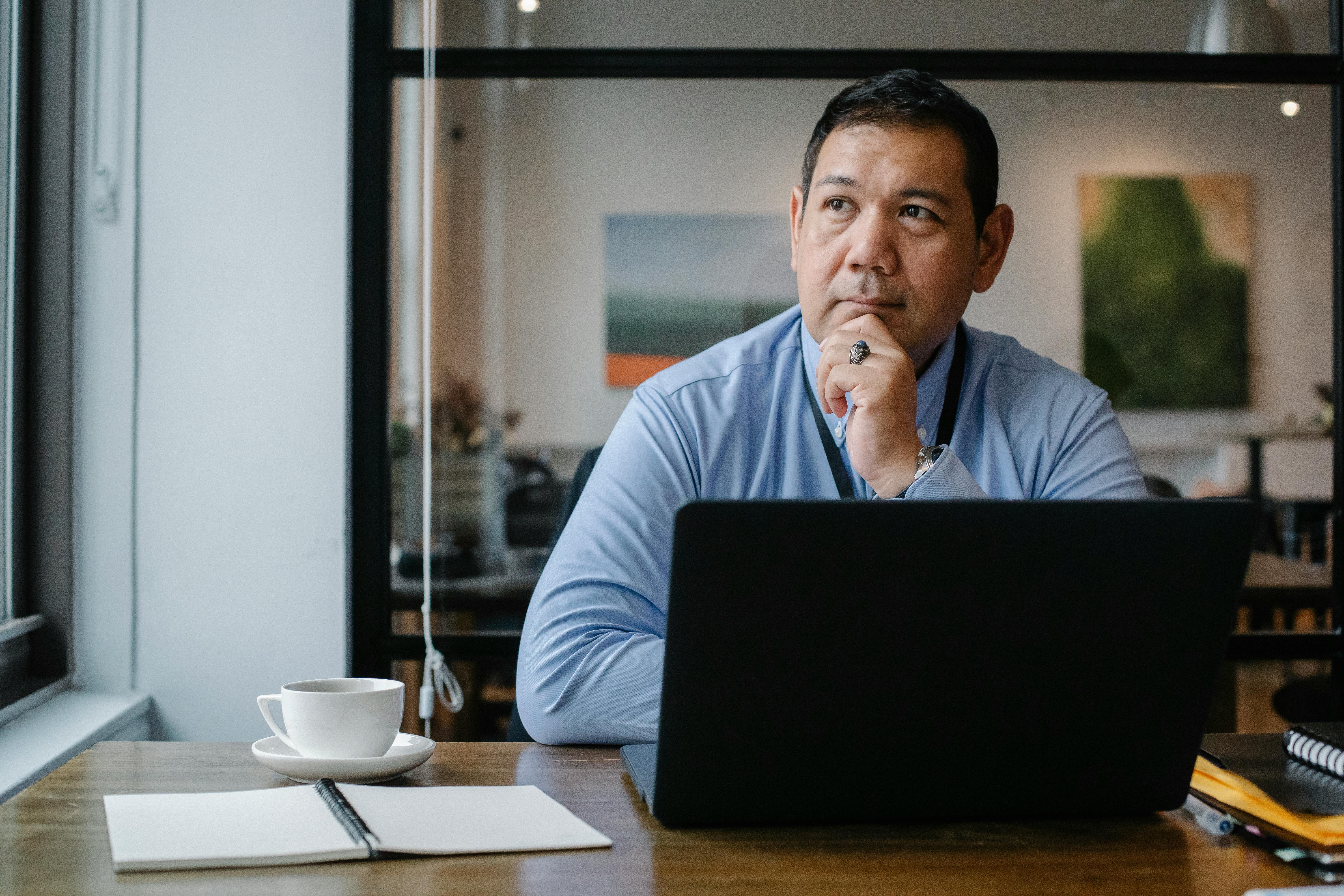 thoughtful ethnic businessman using laptop while working in office