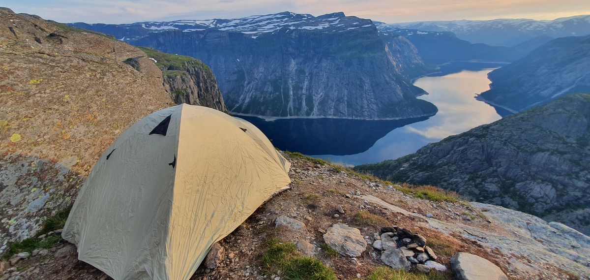 Cort singur pe o margine de stâncă deasupra unui fiord norvegian, la apus
