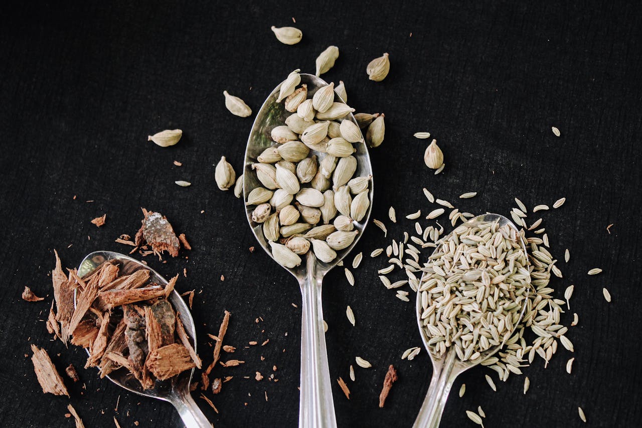 Whole cardamom pods and spices arranged on spoons