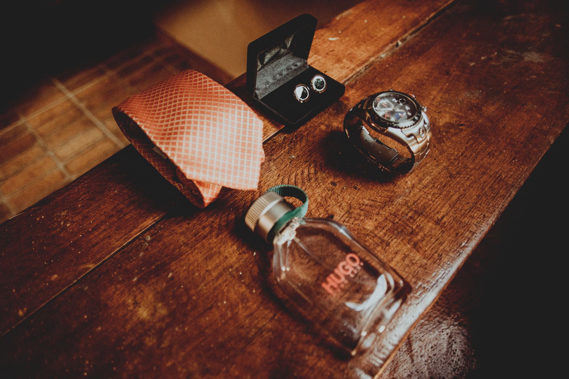 From above composition of silk tie above male perfume bottle and steel watch with cufflinks located on dark wooden surface