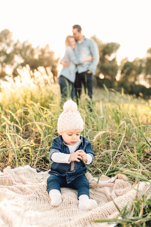 Child in Blue Denim Jacket Sitting on White Knitted Textile