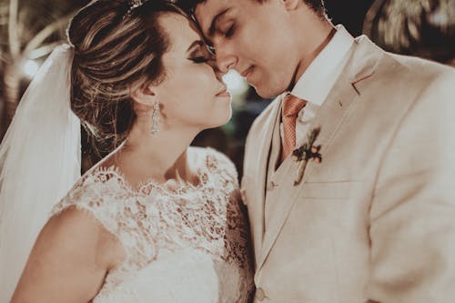 Crop young bride wearing wedding dress and groom touching with foreheads while standing close to each other