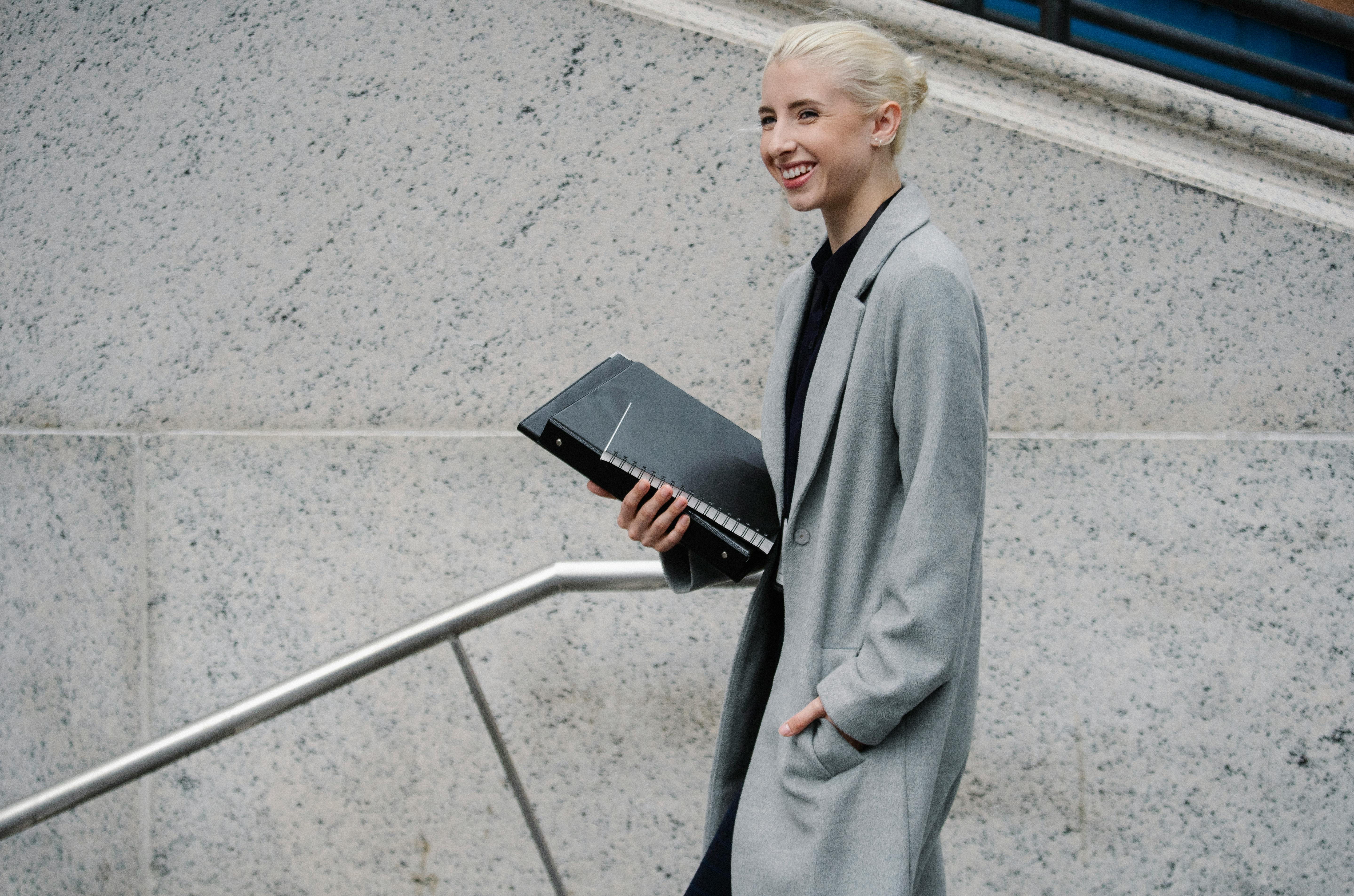 cheerful businesswoman with folders walking on building stairs