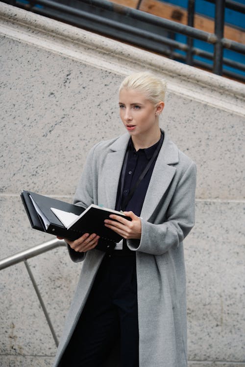 Free From above young concentrated businesswoman in formal clothes standing on street with opened folder and looking away in thoughts Stock Photo