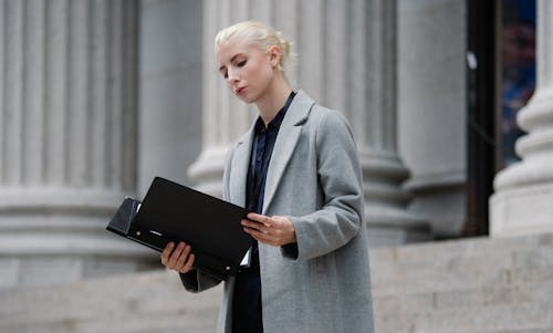 Contemplative businesswoman reading papers in folder outside building