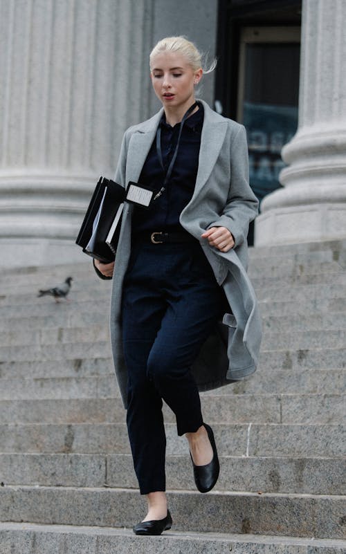 Stylish businesswoman with folders going downstairs outside stone building