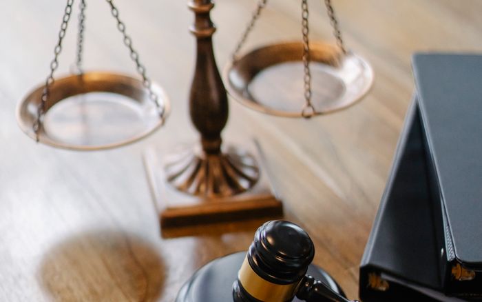 A judge's gavel and brass scales of justice on a wooden desk.
