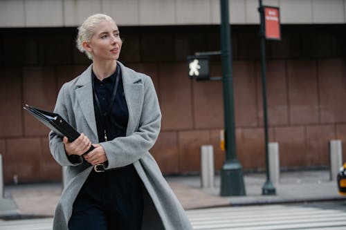 Positive businesswoman crossing road with folders in hands