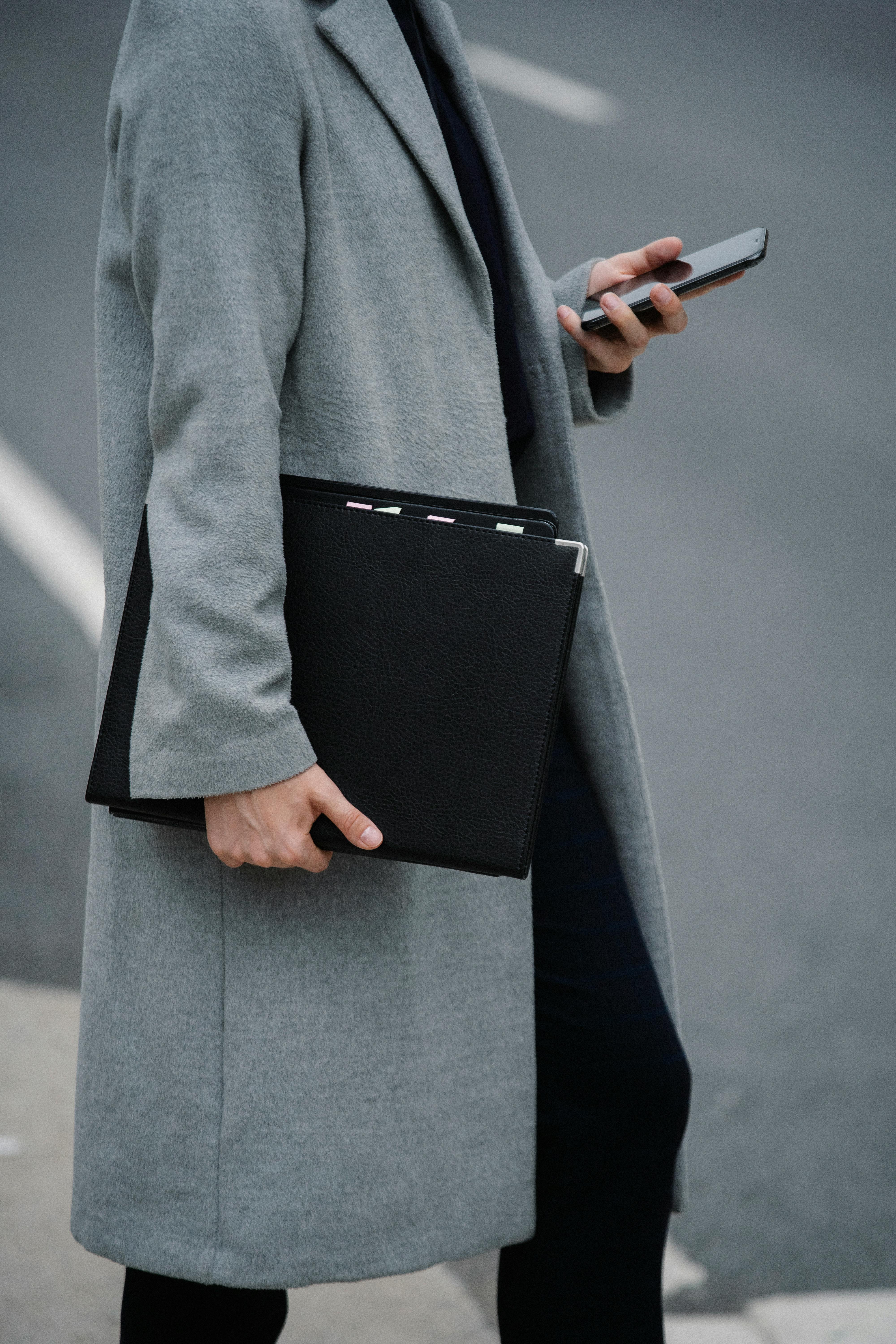 crop faceless woman with paper folder using smartphone on roadside