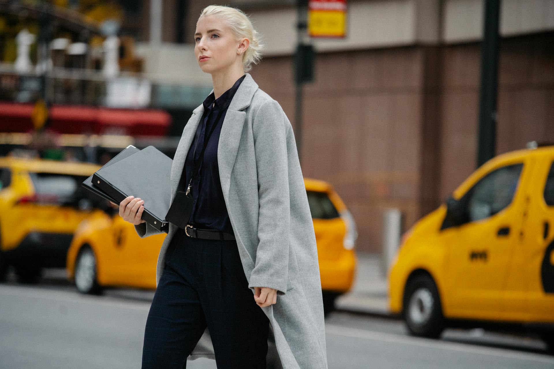 A professional woman in a grey coat crossing a New York City street, showcasing urban business lifestyle.