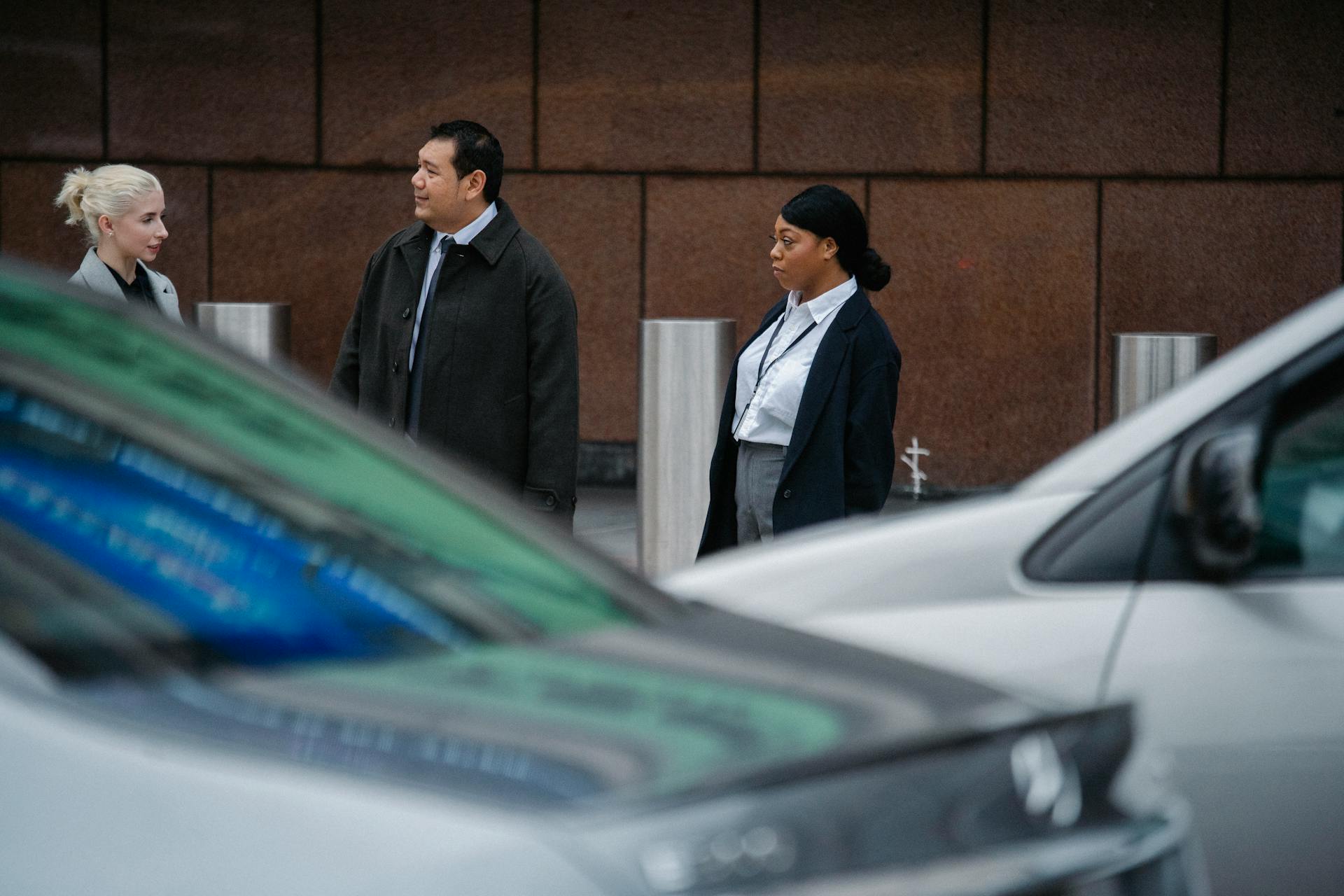 Serious multiracial coworkers wearing formal clothes standing on roadside against office building and discussing business ideas