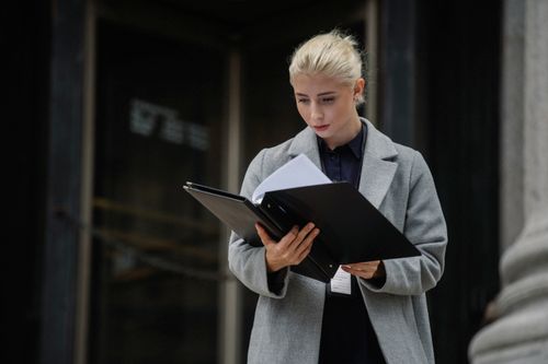 Free Focused young businesswoman in formal clothes standing outside modern building and reading notes in folder Stock Photo