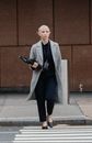Full body confident young businesswoman in elegant formal wear carrying document folders and crossing road in downtown while looking away thoughtfully