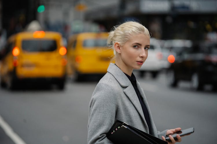 Serious Woman With Smartphone Standing On Busy Street