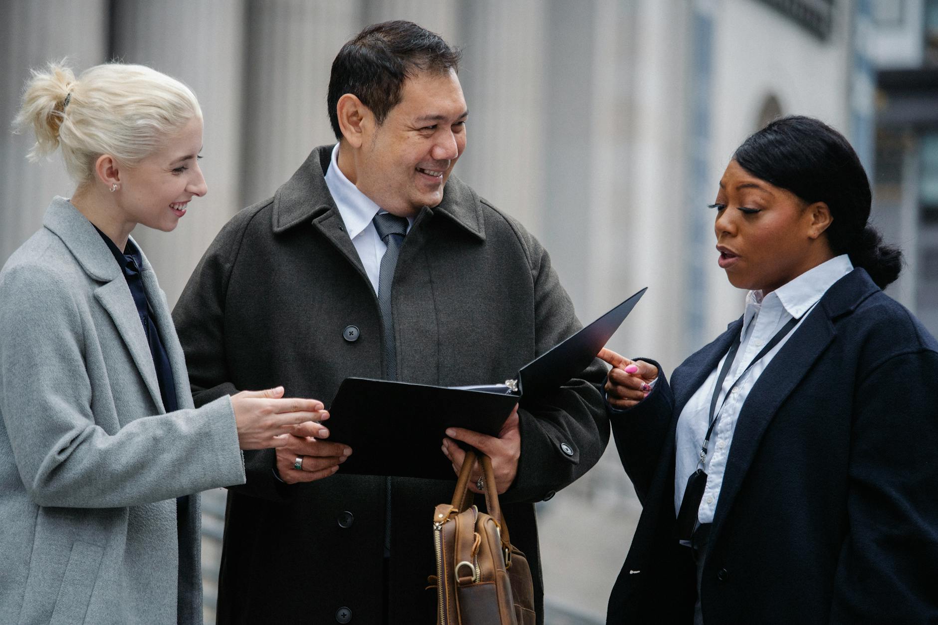 Smiling multiracial coworkers wearing formal outfits standing on street with paper folder and discussing business project together. entry level project manager jobs.